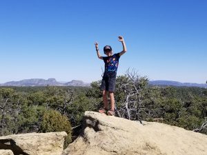 child standing on a New Mexico mountaintop with arms raised triumphantly