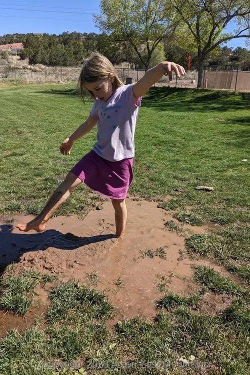 A girl standing barefoot in a mud puddle. 