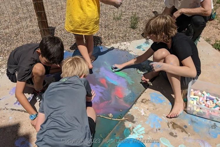 Learners at Acton Academy East Mountains private school in Cedar Crest, New Mexico playing outside with chalk and water on the sidewalk.